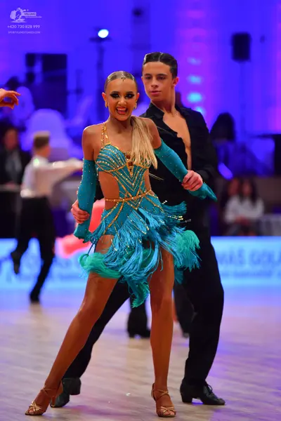 Dancesport competitor: Female dancer: teal Latin dress with gold sequined/beaded patterns and long frin