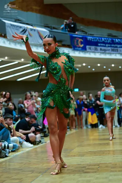 Dancesport competitor: Female dancer 1: emerald green latin dance dress with sequins, cutouts, and long