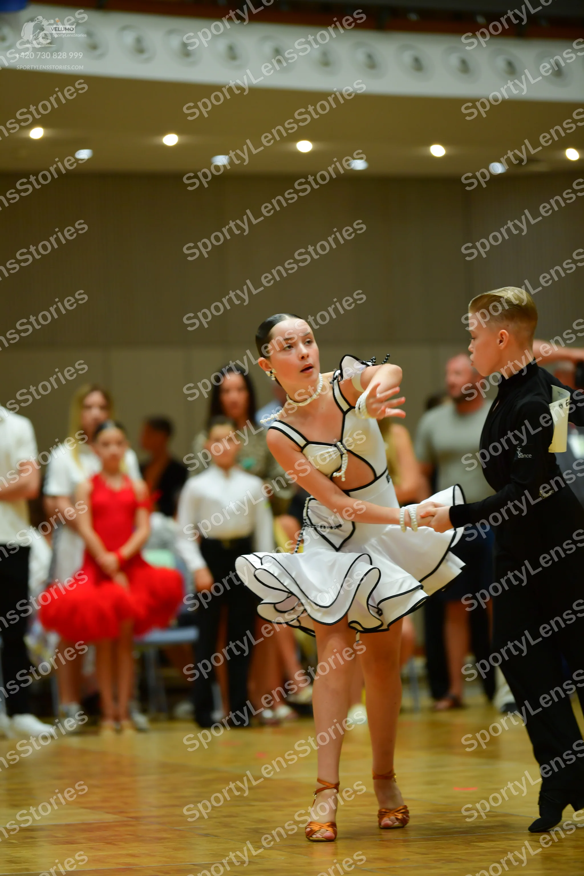 Dancesport competitor: Main female dancer: white latin dress with black trim and a ruffled, flared skir