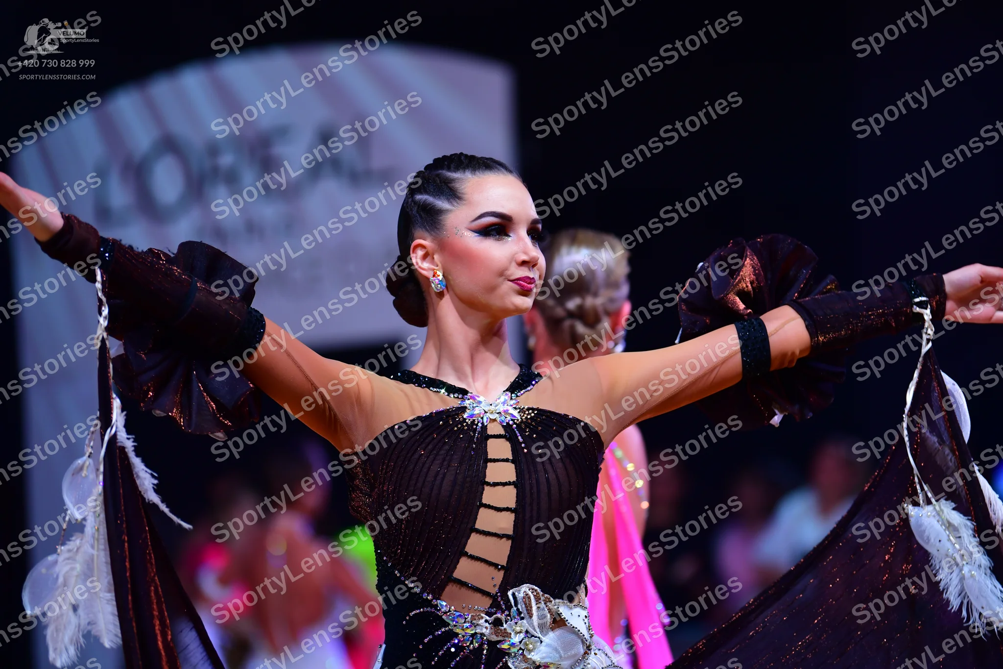 Dancesport competitor: Female dancer in foreground: dark brown/black latin dance dress with sheer nude-