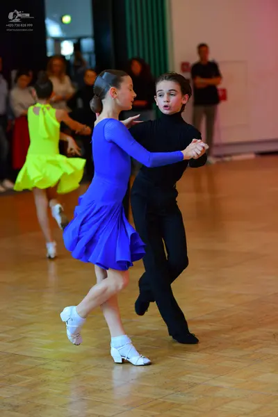 Dancesport competitor: Female dancer in foreground: blue long-sleeved latin dress with a flared skirt a