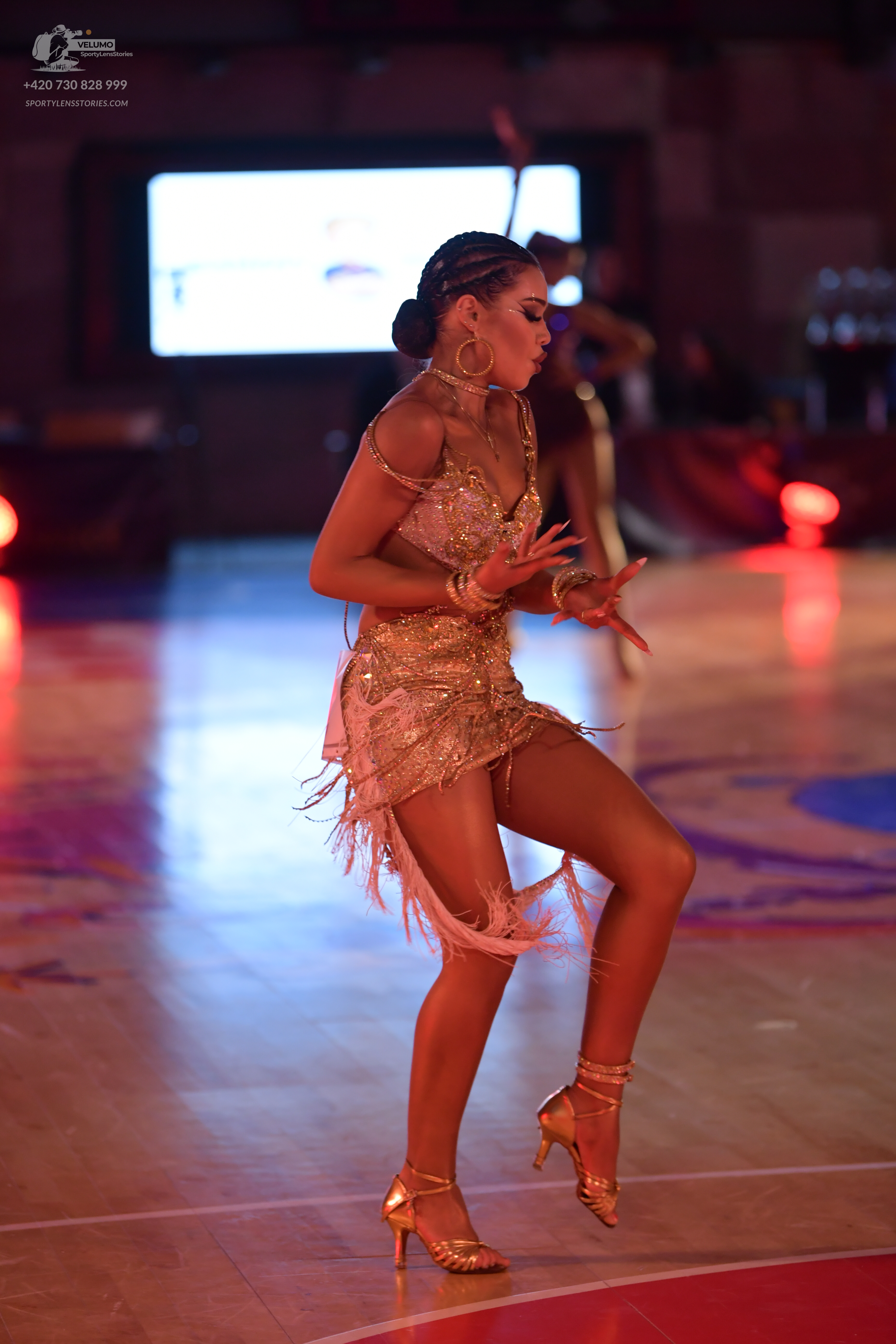 Dancesport competitor: Female dancer: gold sequin Latin dress with fringe, gold bracelets, and gold dan