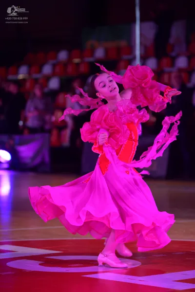 Dancesport competitor: Female dancer: bright pink Latin dress with voluminous ruffled sleeves and a flo