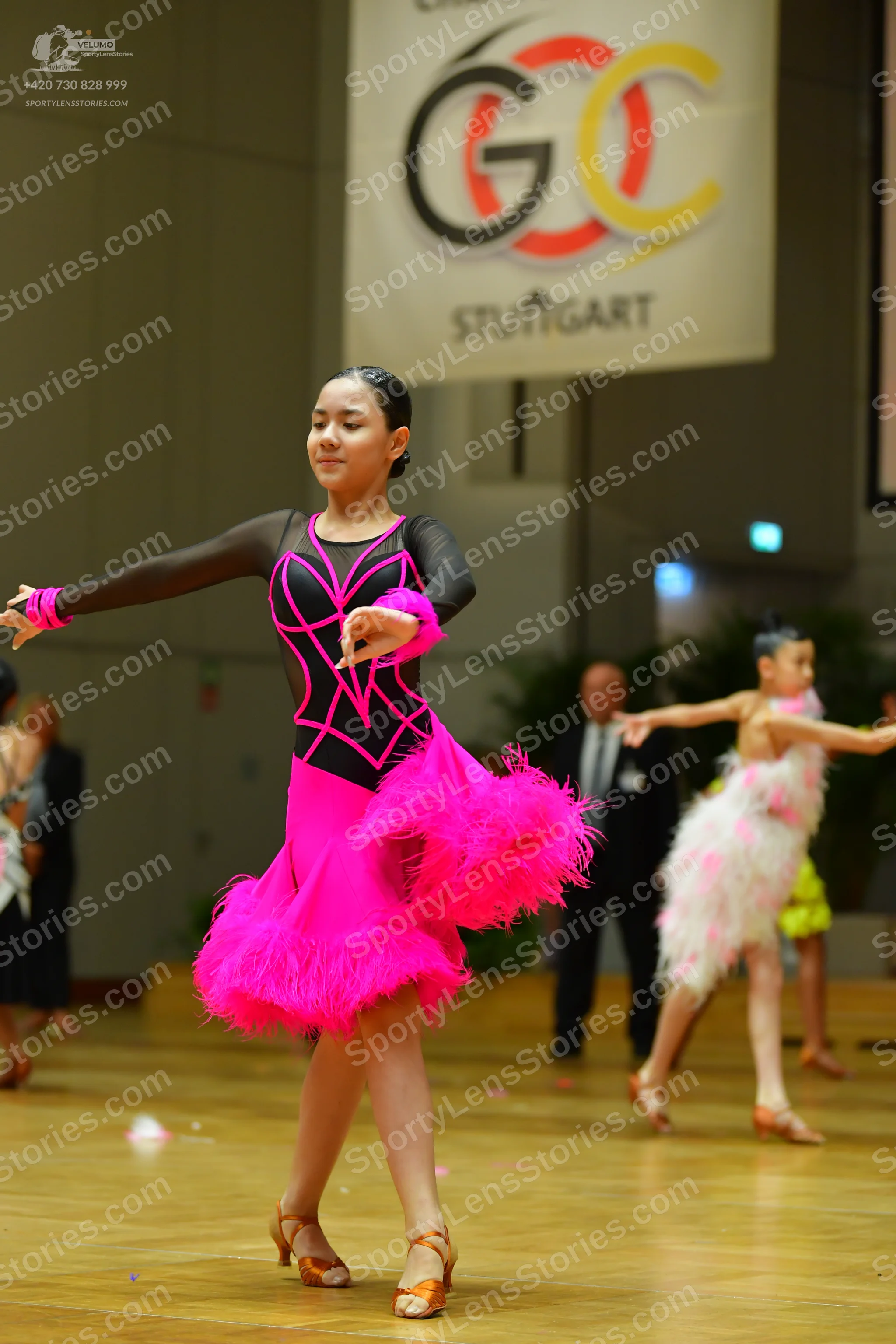 Dancesport competitor: Female dancer in foreground: black long-sleeved Latin dress with bright pink pip