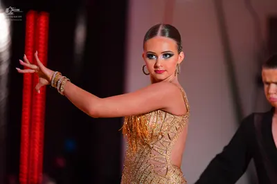 Dancesport competitor: Female dancer: gold latin dress with sequins, mesh, and fringe, accessorized wit