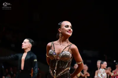Dancesport competitor: Main female dancer: dark brown or black Latin dance costume with extensive gold 