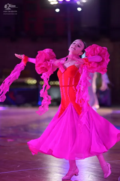 Dancesport competitor: Female dancer: bright pink/magenta Latin dress with a fitted bodice and a flowin