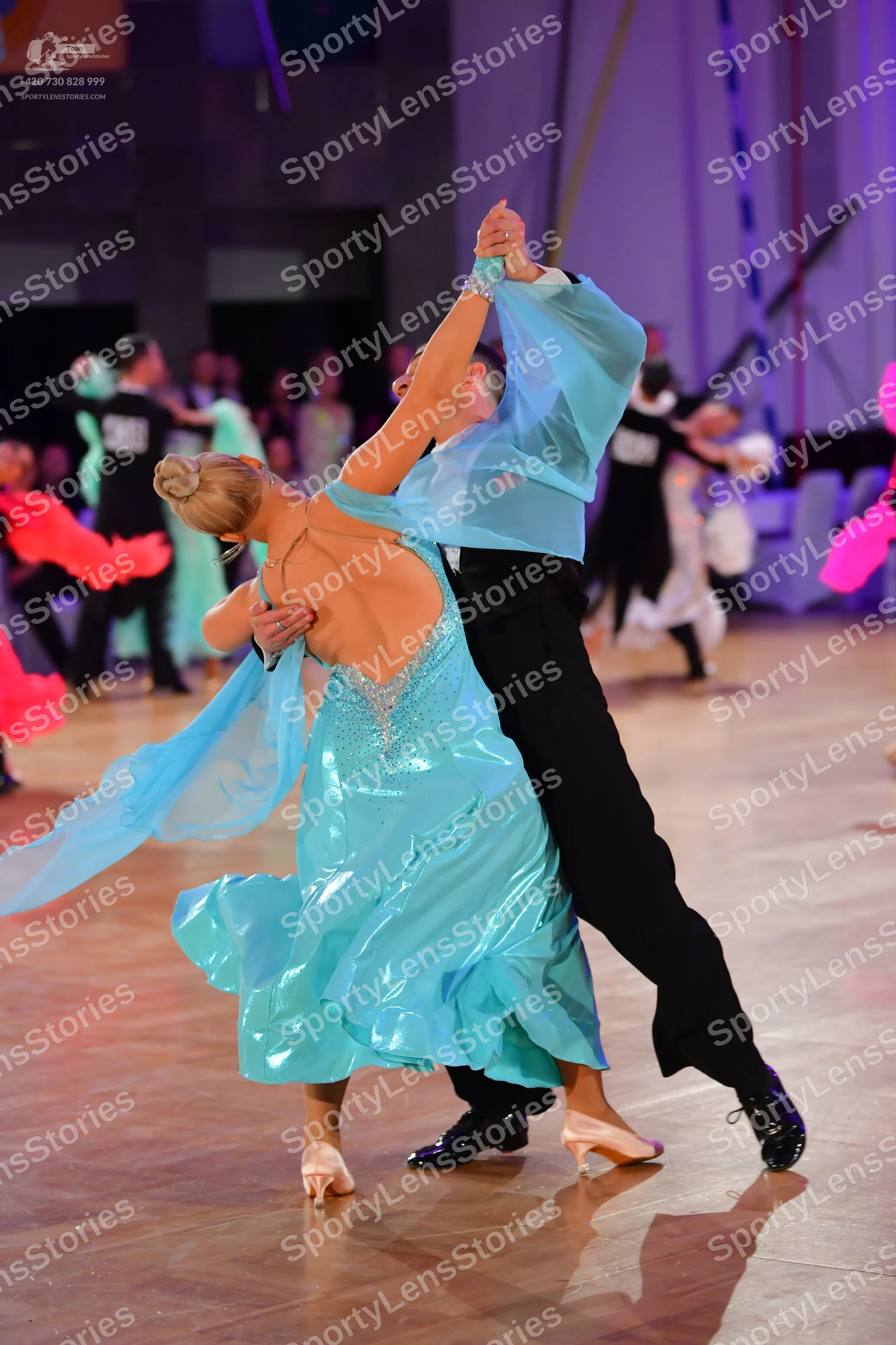 Dancesport competitor: Female dancer: light blue/cyan satin latin dress with sheer, flowing sleeves and