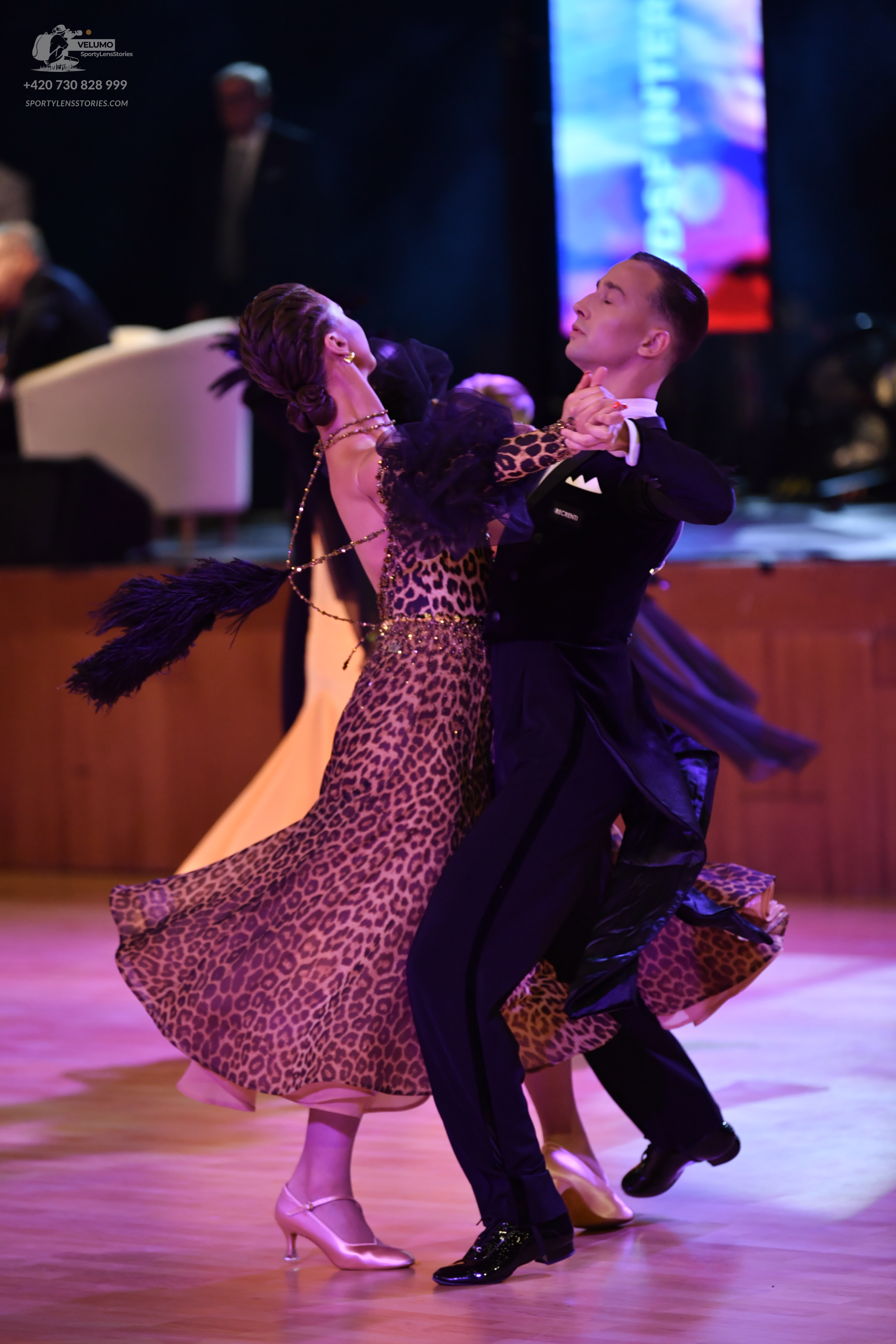 Dancesport competitor: Female dancer: leopard print ballroom dress with black feather-like accents on t