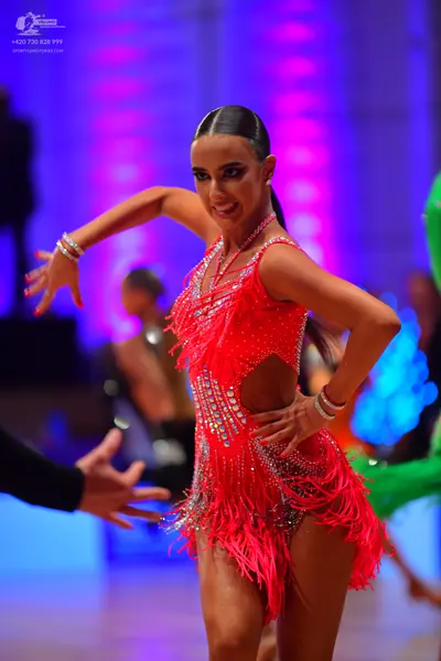 Dancesport competitor: Female dancer: red Latin dress with red fringe, sequins, and rhinestones, featur