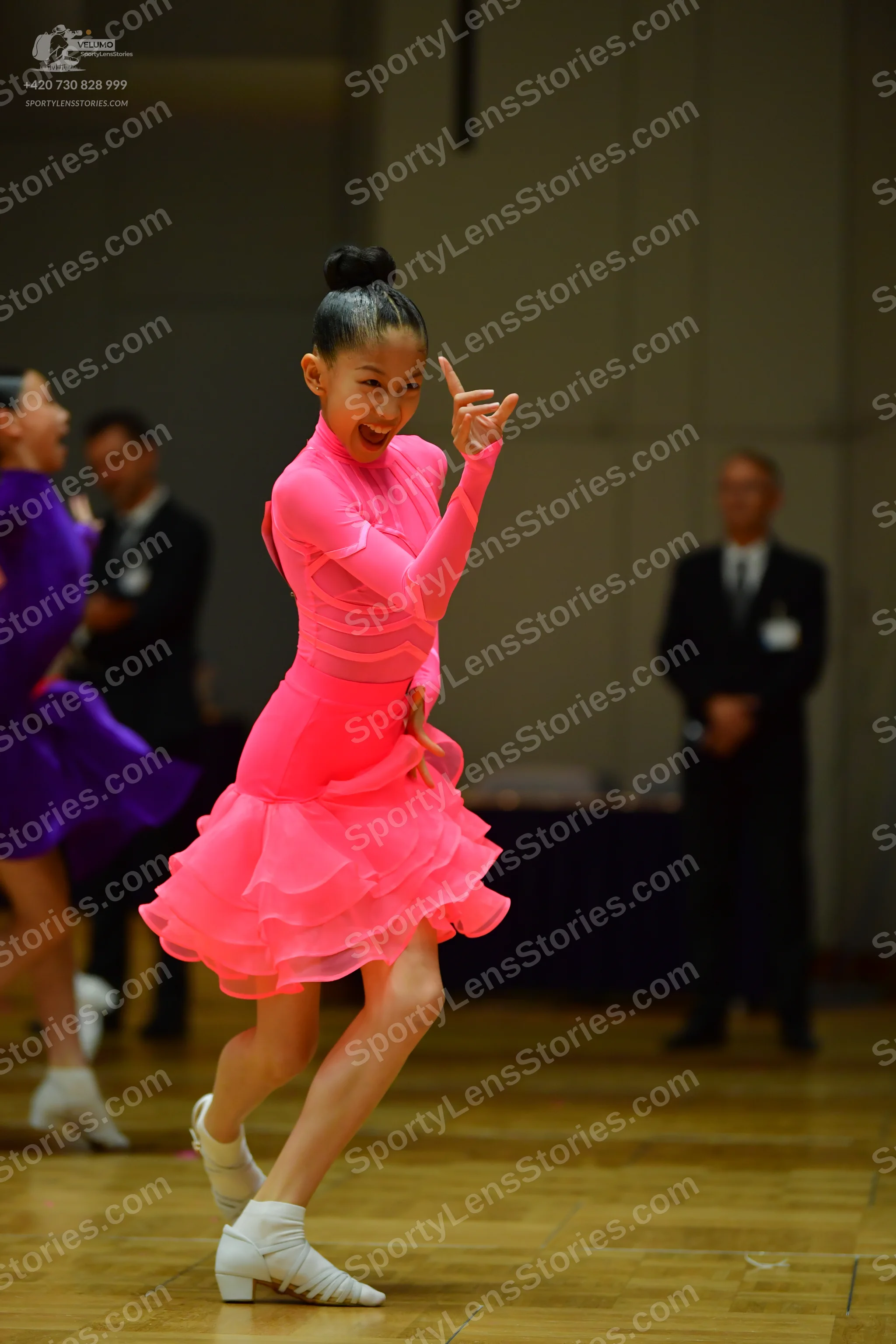 Dancesport competitor: Female dancer in foreground: bright pink long-sleeved latin dance dress with a l