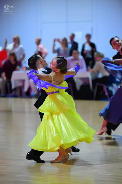 Dancesport competitor: Female dancer: bright yellow ballgown with a purple and blue bodice and a shimme