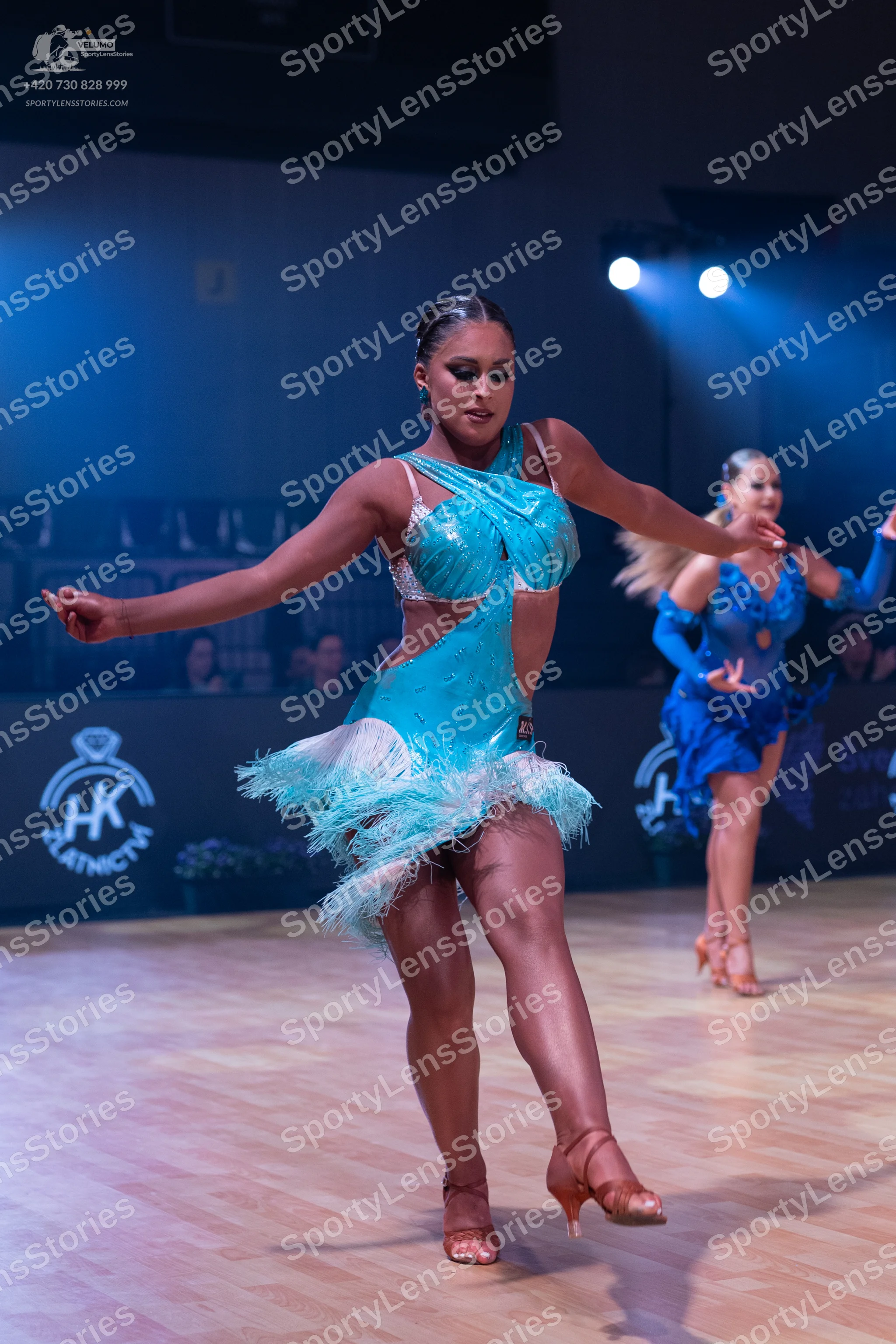 Dancesport competitor: Female dancer in foreground: turquoise latin dress with sequins and feather/frin