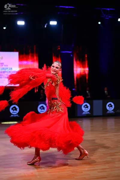 Dancesport competitor: Female dancer: red latin dress with red feathers on the sleeves and skirt, and g