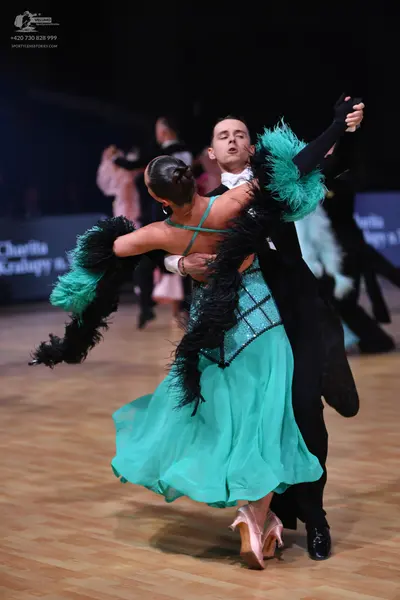 Dancesport competitor: Female dancer: teal latin dress with black feather/fringe trim on the sleeves an
