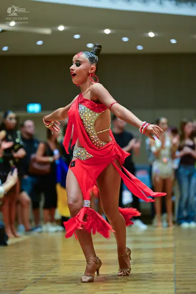 Dancesport competitor: Female dancer: red latin dress with gold and silver sequins, featuring an asymme
