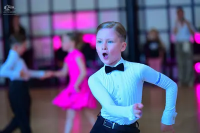 Dancesport competitor: Male dancer in foreground: white long-sleeved textured shirt, black bow tie, and