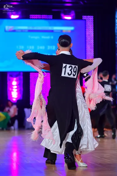 Dancesport competitor #139: Male dancer: black long-sleeved shirt and black trousers, holding a large, light
