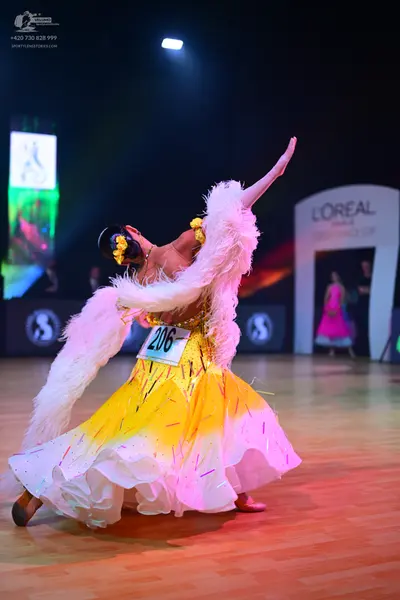 Dancesport competitor: Female dancer: yellow and white voluminous skirt with a large white feather boa 