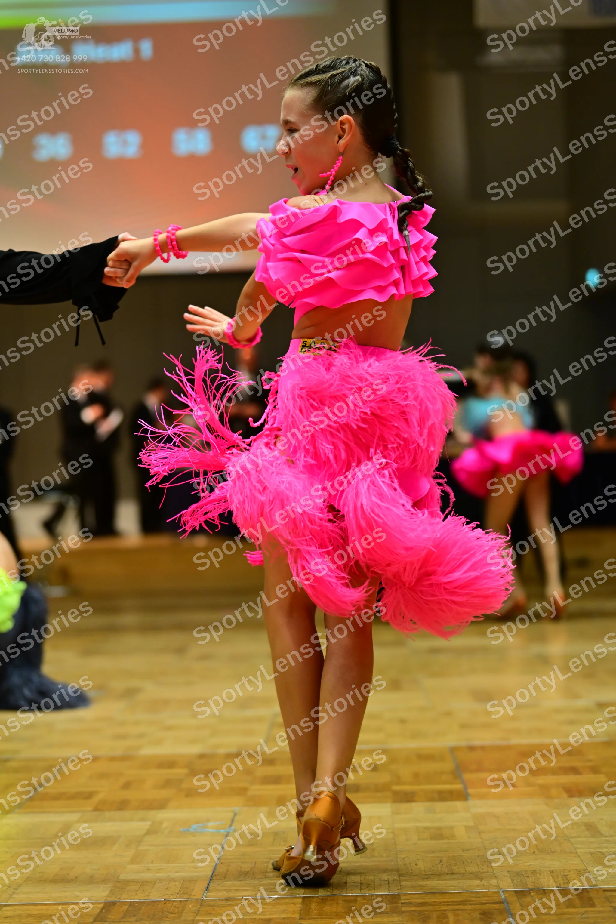 Dancesport competitor: Female dancer in foreground: bright pink Latin dance costume featuring a ruffled