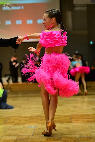 Dancesport competitor: Female dancer in foreground: bright pink Latin dance costume featuring a ruffled