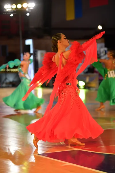 Dancesport competitor #11: Female dancer in foreground: red latin dress with ruffled, flowing sleeves and a