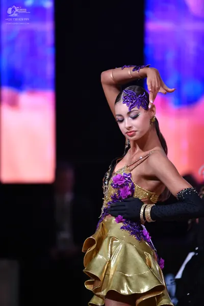 Dancesport competitor: Female dancer: gold satin Latin dress with purple floral lace appliqués and a la