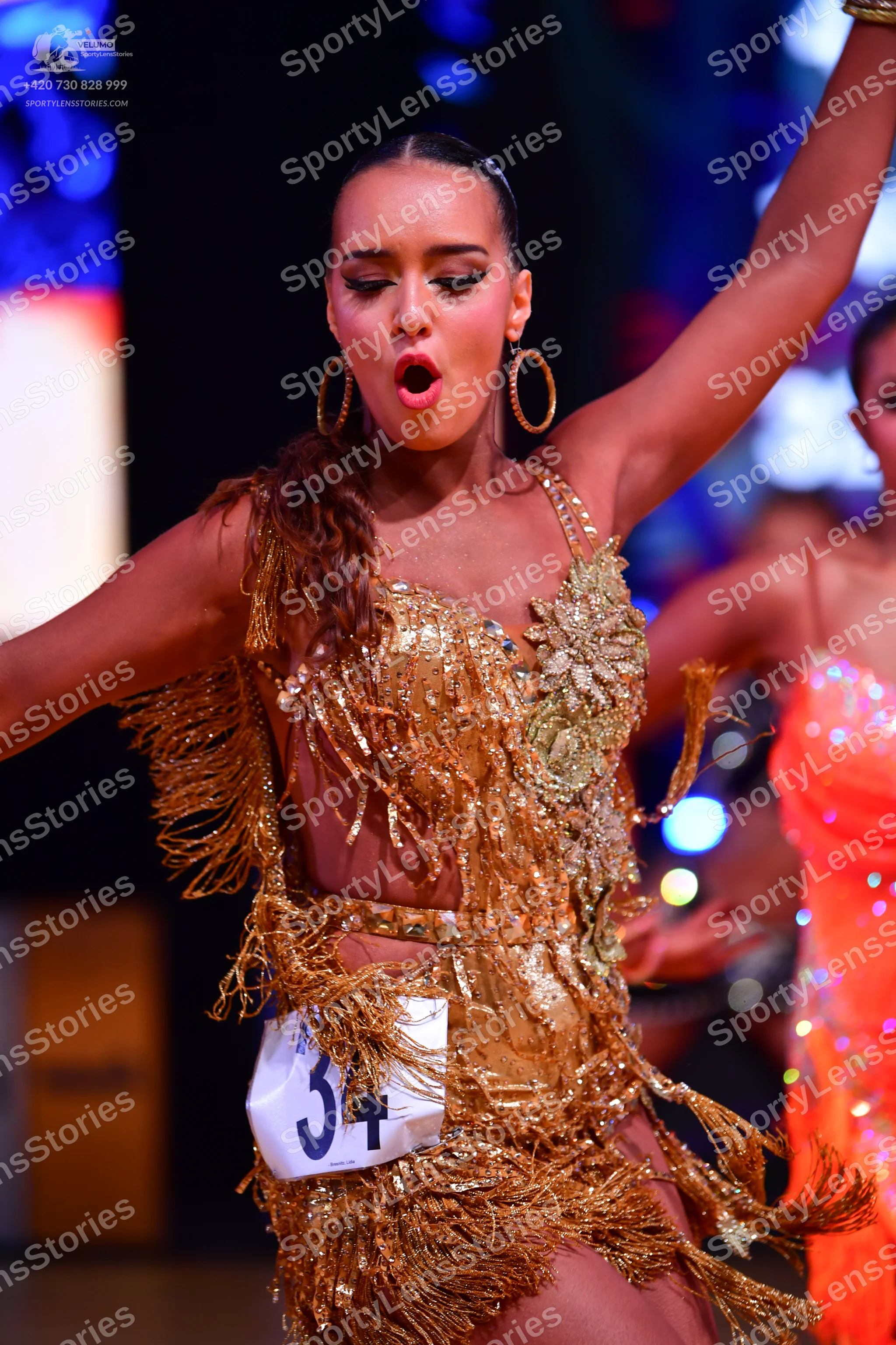 Dancesport competitor: Primary dancer: gold sequin and fringe Latin dress with large gold hoop earrings