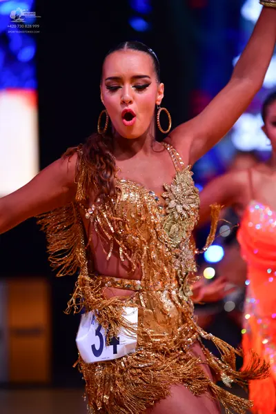Dancesport competitor: Primary dancer: gold sequin and fringe Latin dress with large gold hoop earrings