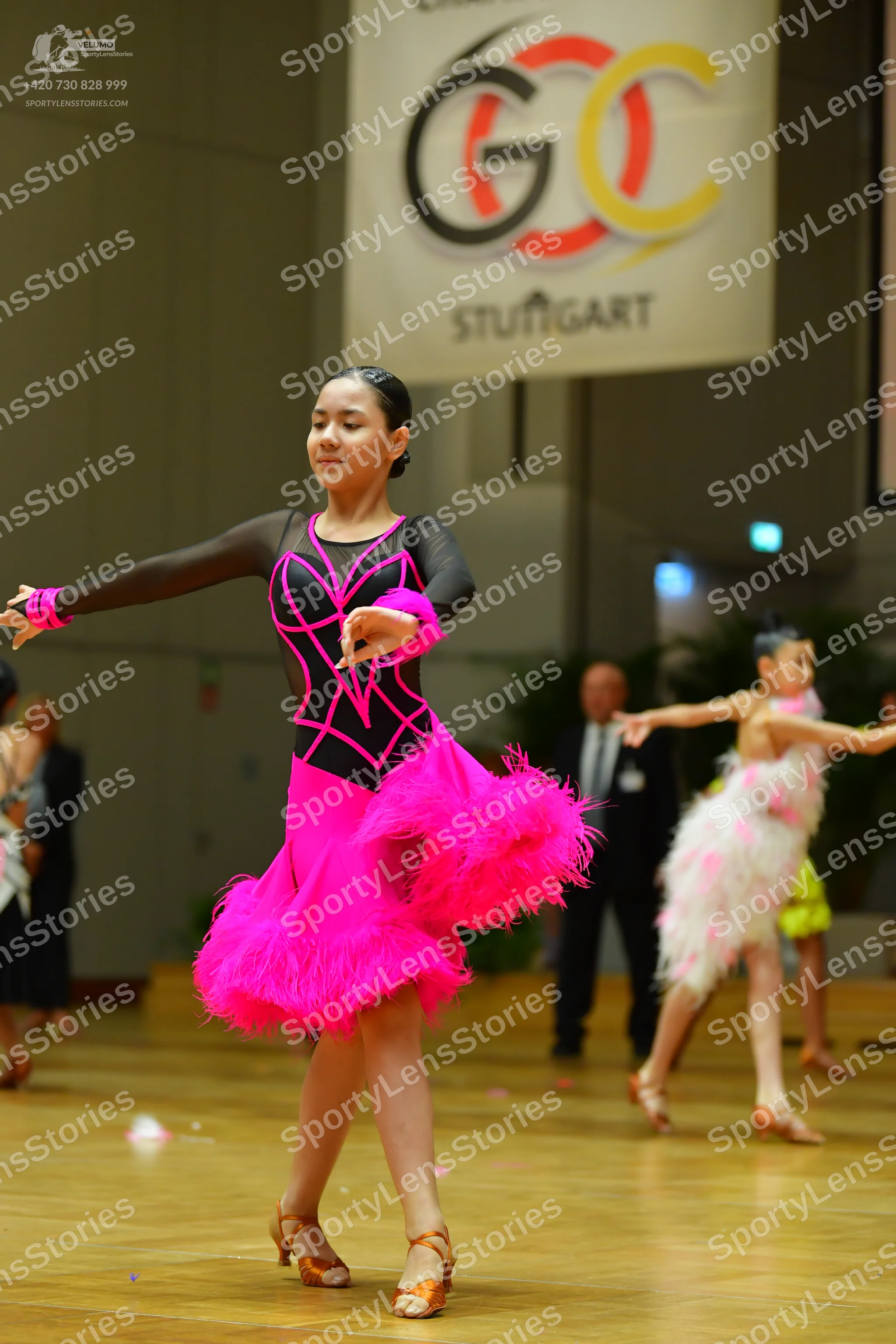 Dancesport competitor: Central female dancer: black long-sleeved Latin dress with bright pink piping on