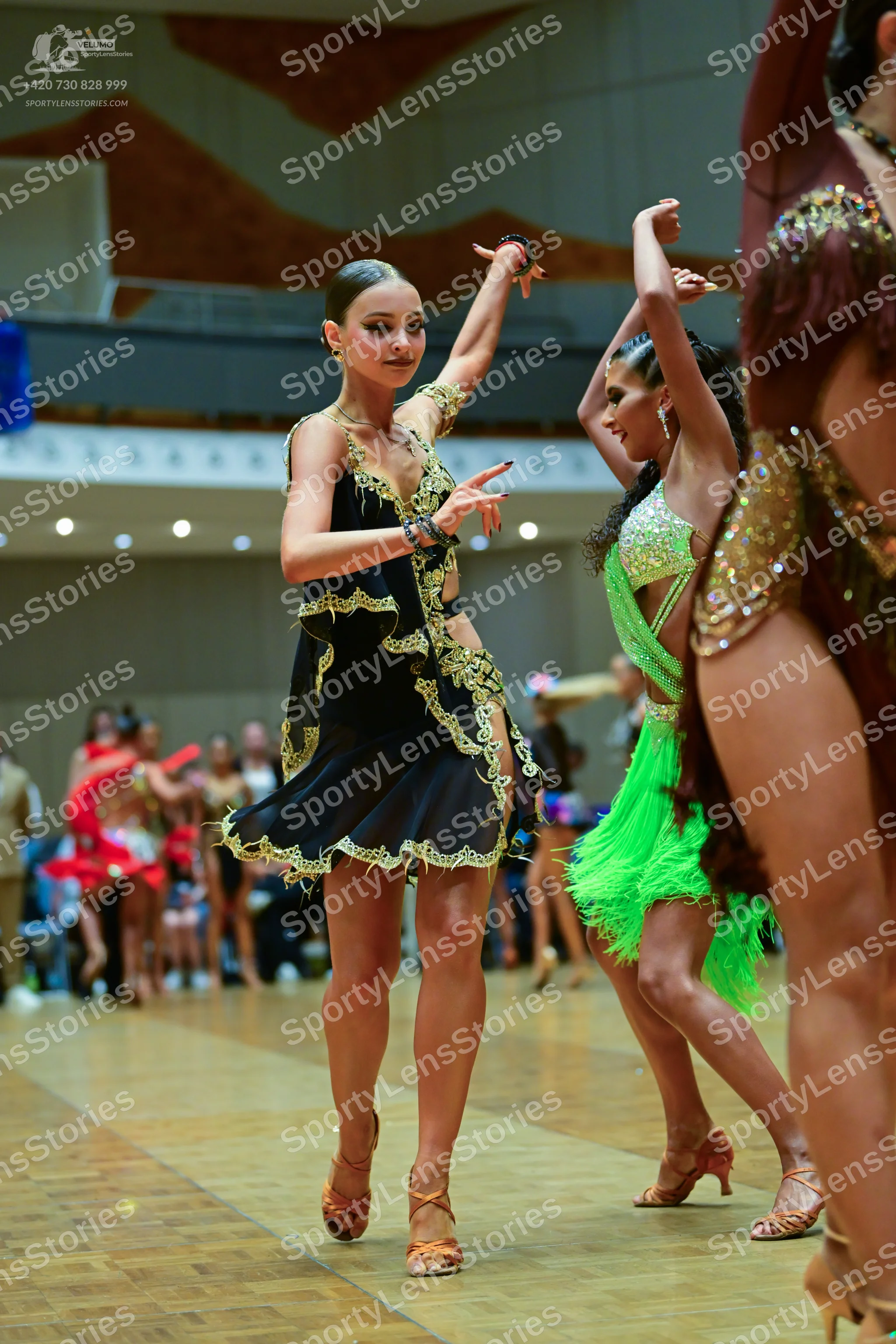 Dancesport competitor: Female dancer: black latin dress with gold lace trim, gold earrings, and black b