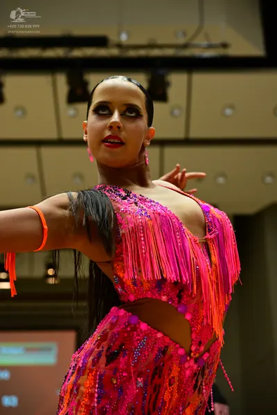 Dancesport competitor: Female dancer: bright pink and orange latin dress with fringe, sequins, and mesh