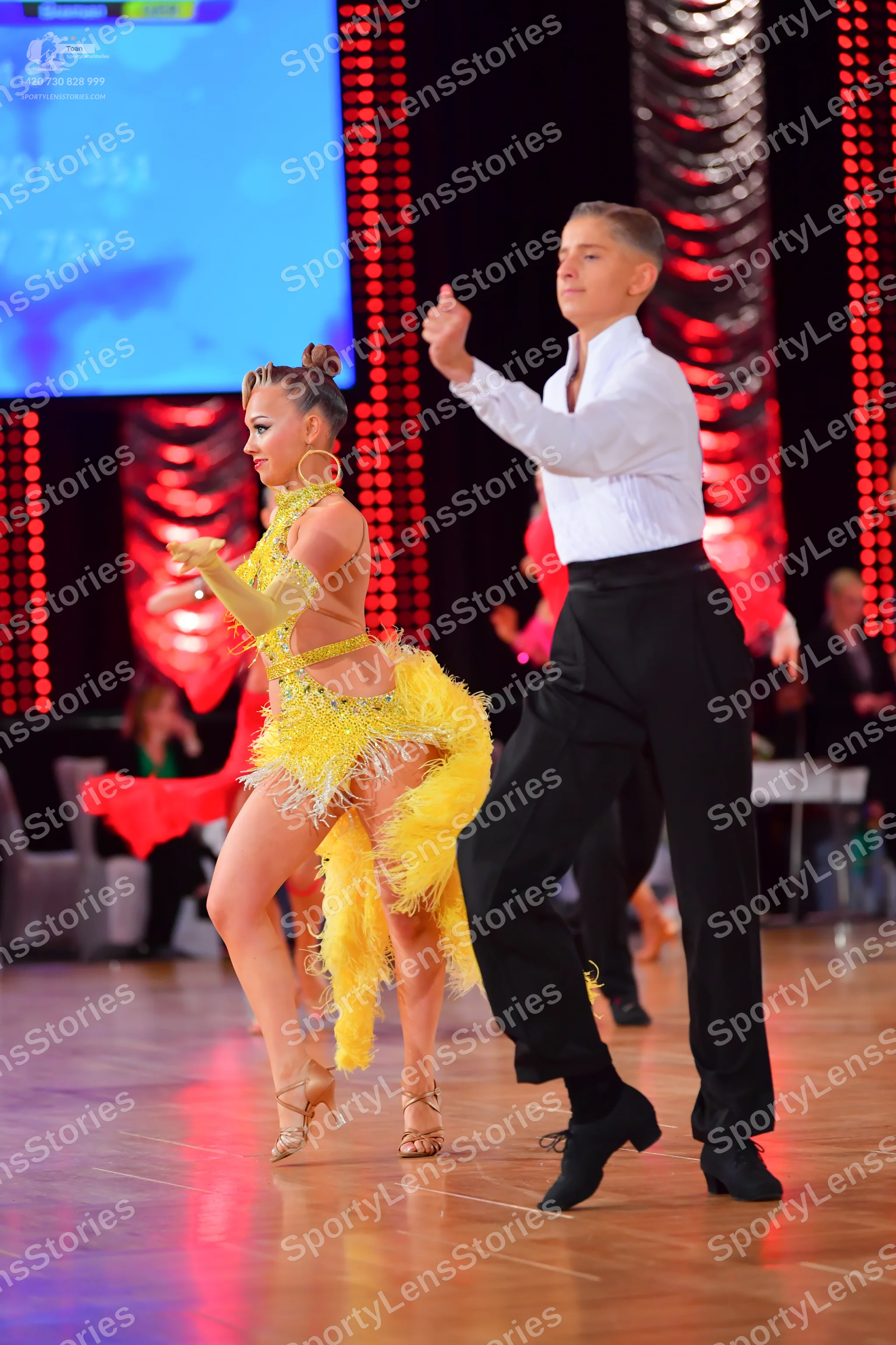 Dancesport competitor: Female dancer: yellow latin dress with fringe, gold long gloves, and large gold 