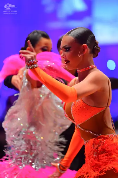 Dancesport competitor: Female dancer in foreground: orange latin dress with sequins, fringe, long sleev