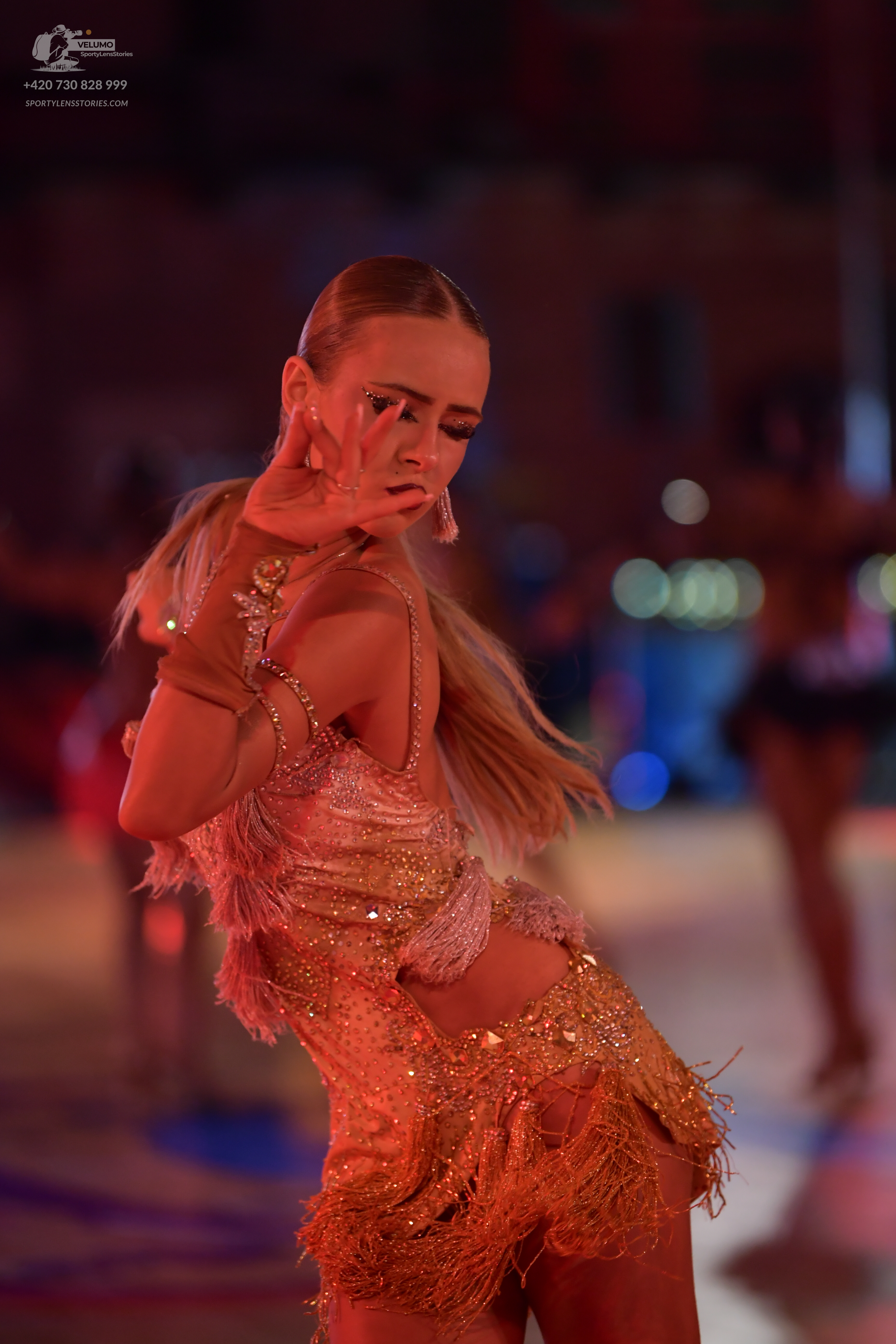 Dancesport competitor: Female dancer: gold sequin latin dress with fringe and cutouts, accessorized wit