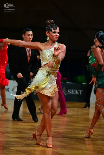 Dancesport competitor: Female dancer in foreground: gold and cream two-piece Latin costume with sequins