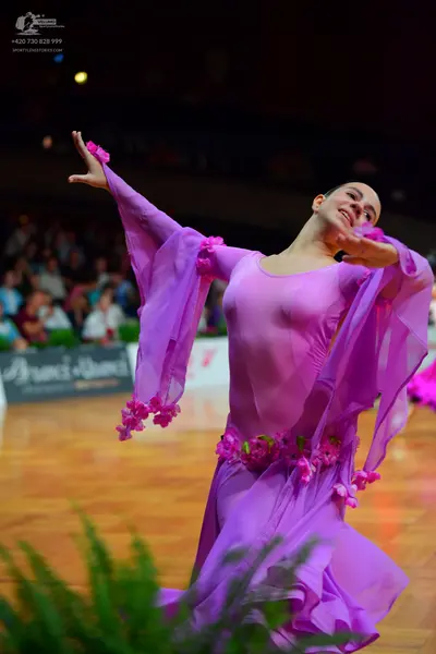 Dancesport competitor: Female dancer: purple ballroom dress with flowing, translucent sleeves and a lon
