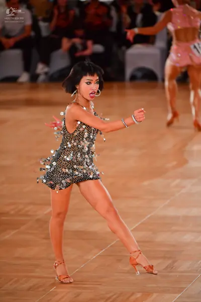 Dancesport competitor: Female dancer in foreground: dark grey/black Latin dance dress covered in large 