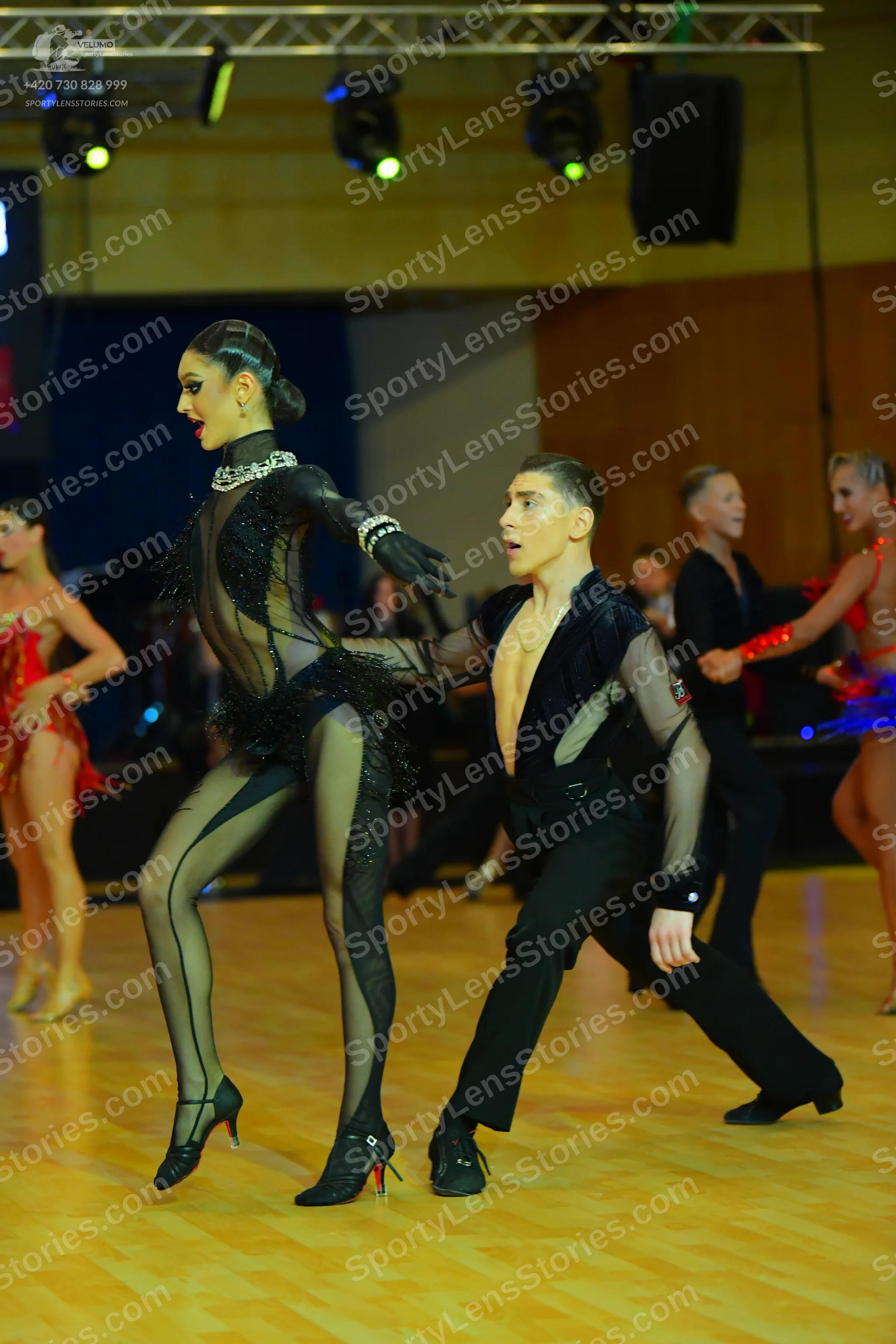 Dancesport competitor: Female dancer in foreground: black sheer/mesh bodysuit with sequins and fringe, 