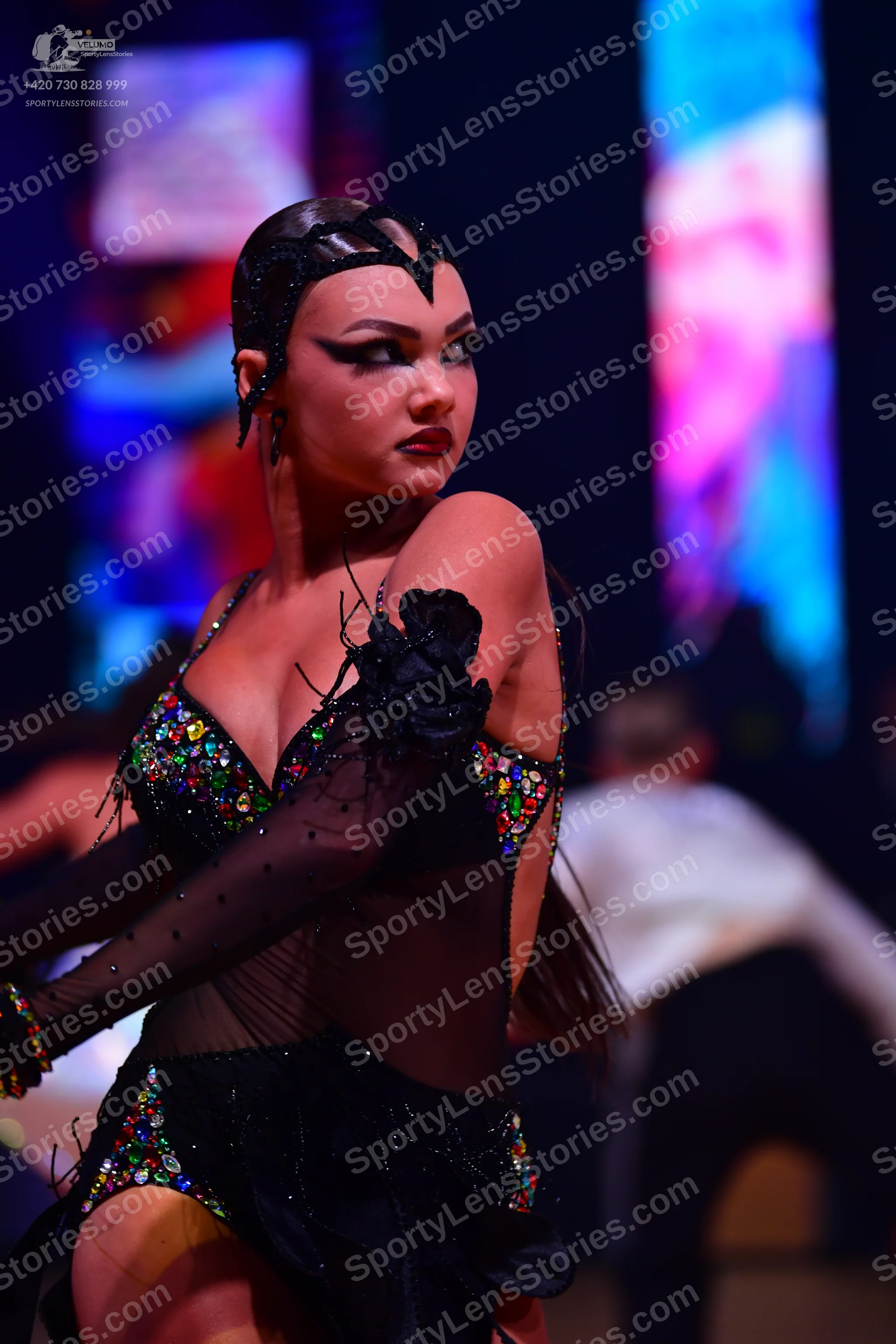 Dancesport competitor: Female:** Black, form-fitting latin dress with intricate, multi-colored (red, go