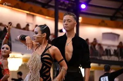 Dancesport competitor #24: Female dancer in foreground: black Latin dance costume with gold sequins and fri