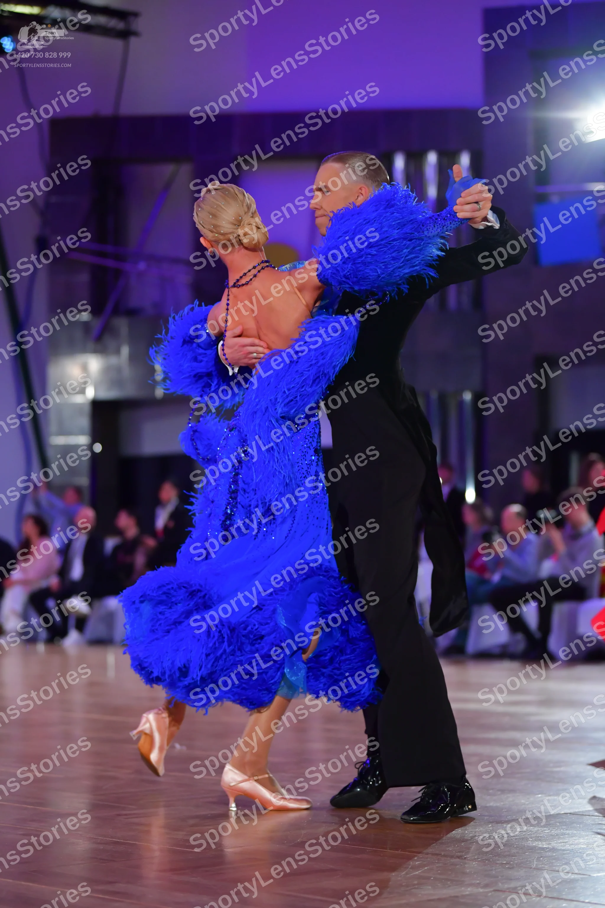 Dancesport competitor: Female dancer: bright blue feathered latin dress with a long dark beaded necklac