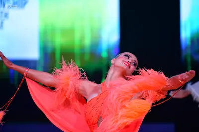 Dancesport competitor: Female dancer: orange/coral Latin dance dress with large feather embellishments