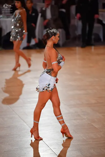 Dancesport competitor: Female dancer in foreground: white and silver Latin dance dress with sequin embe