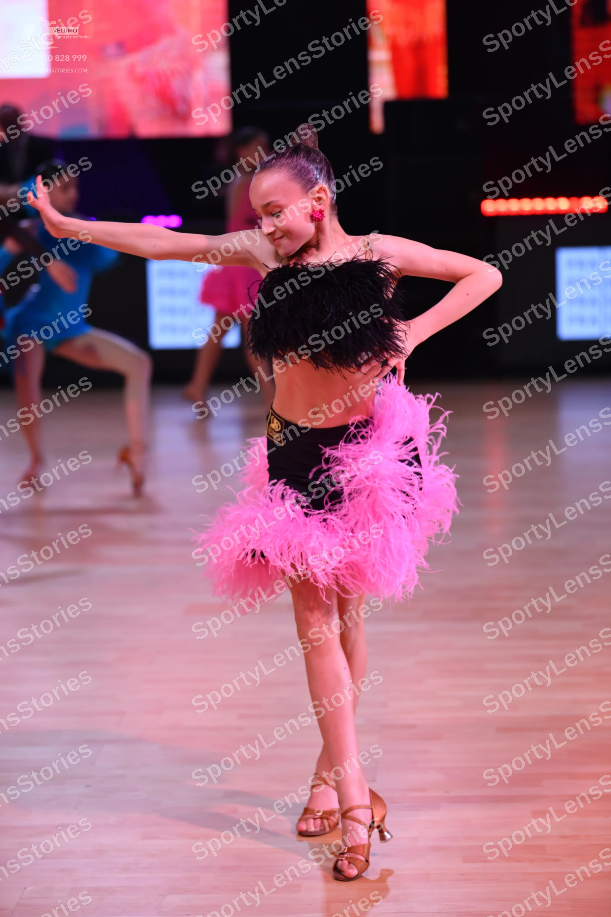 Dancesport competitor: Female dancer in foreground: black feathered top and a voluminous bright pink fe