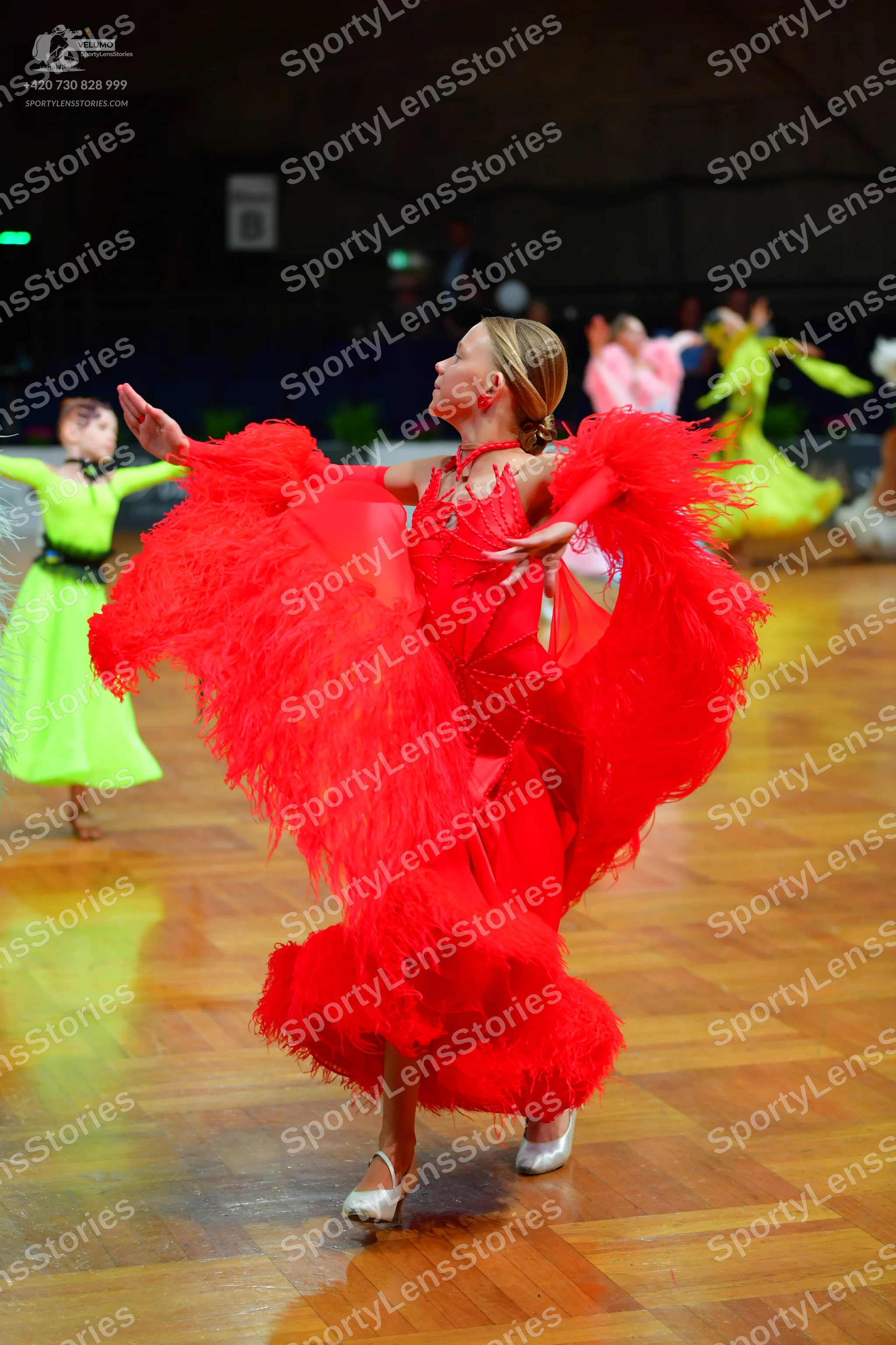 Dancesport competitor: Female dancer (center): red Latin dress with long red fringe on the sleeves and