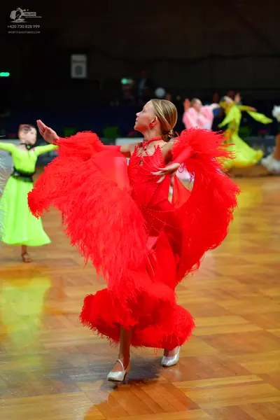 Dancesport competitor: Female dancer (center): red Latin dress with long red fringe on the sleeves and 
