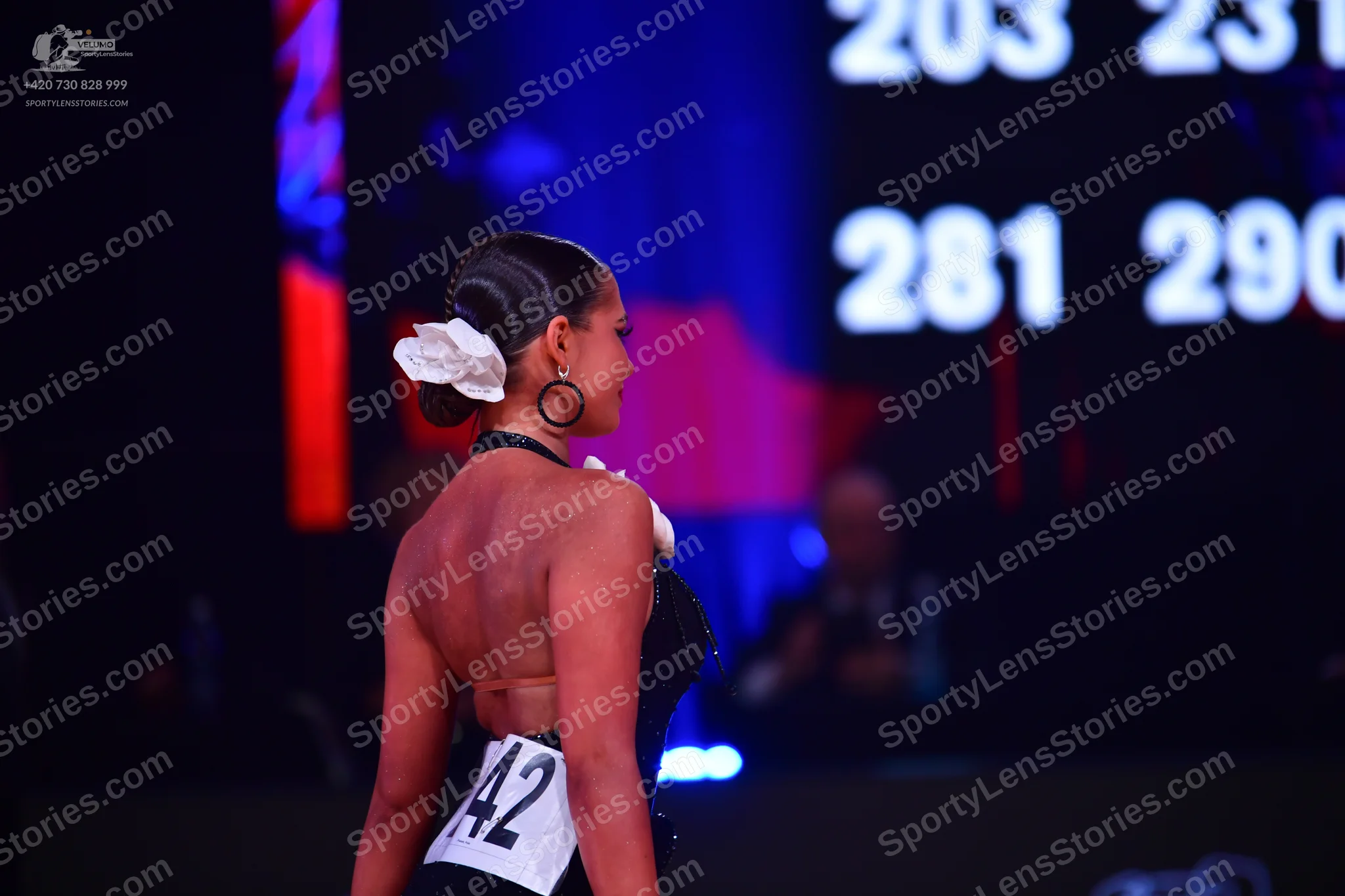 Dancesport competitor: Female dancer: black backless dress with white floral hair accessory and large h