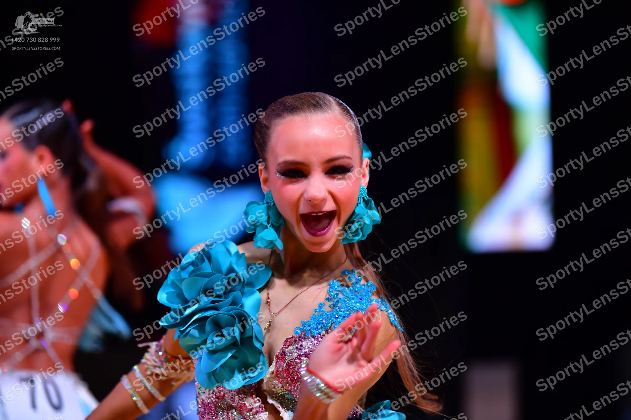Dancesport competitor: Female dancer (foreground): teal and pink/silver Latin dance dress with large te