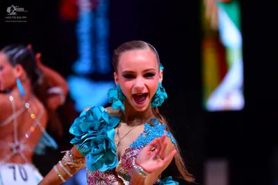 Dancesport competitor: Female dancer (foreground): teal and pink/silver Latin dance dress with large te